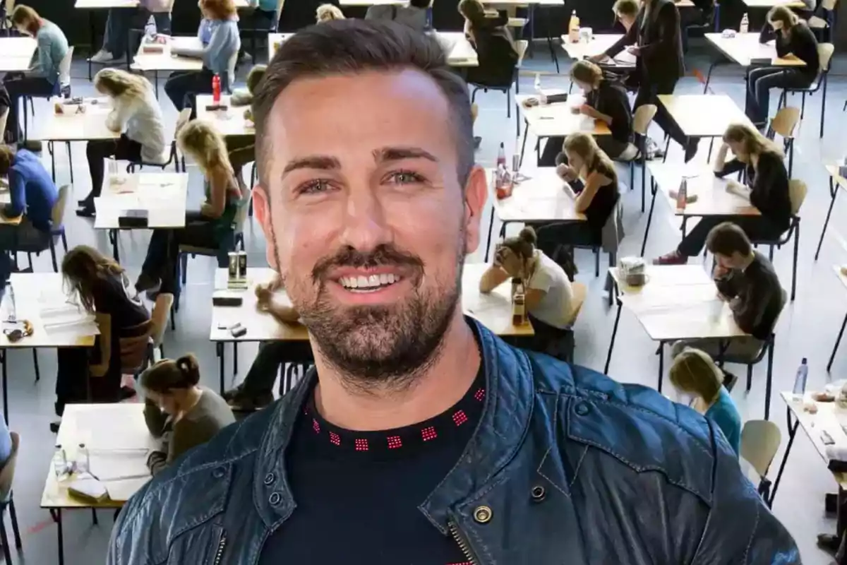 Un hombre sonriente con chaqueta de cuero frente a un aula llena de estudiantes tomando un examen.