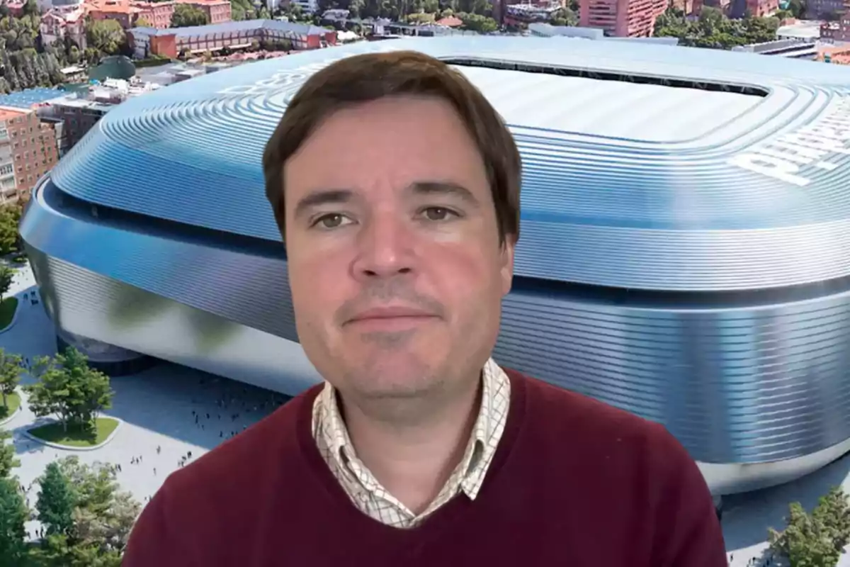 Un hombre con suéter burdeos frente a un estadio moderno.