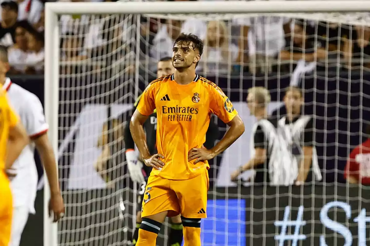 Jugador de fútbol con uniforme naranja del Real Madrid en el campo de juego con expresión de frustración.