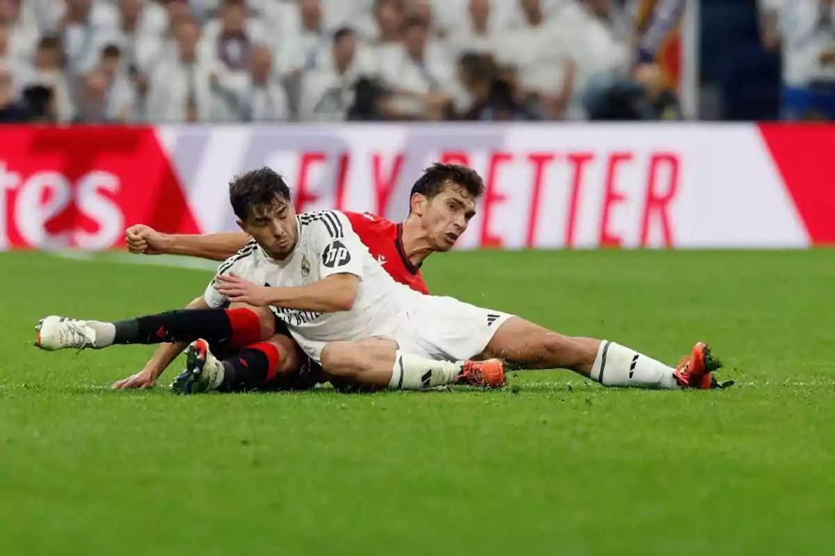 Dos jugadores de fútbol compiten por el balón en el suelo durante un partido.