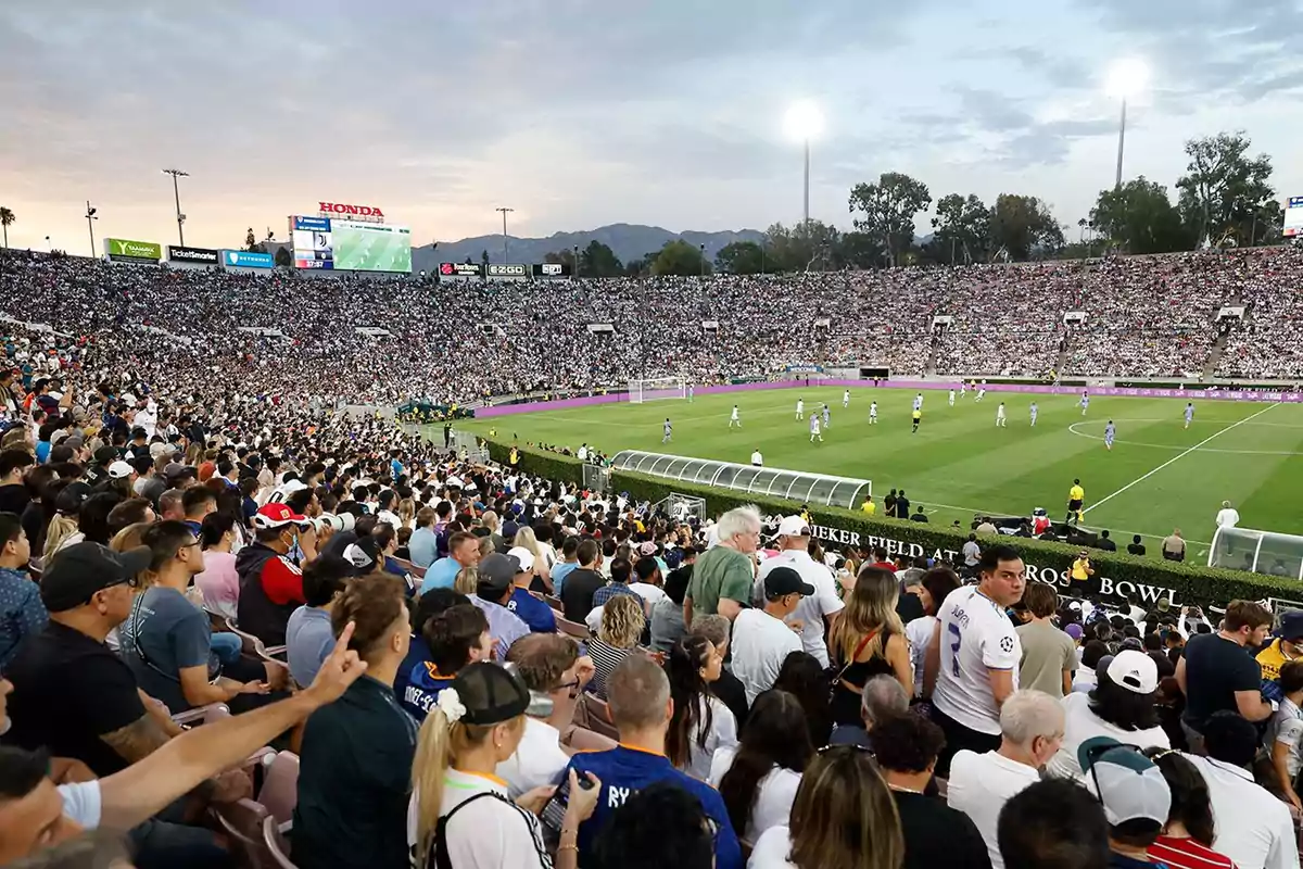 Estadio lleno de aficionados durante un partido de fútbol al atardecer.