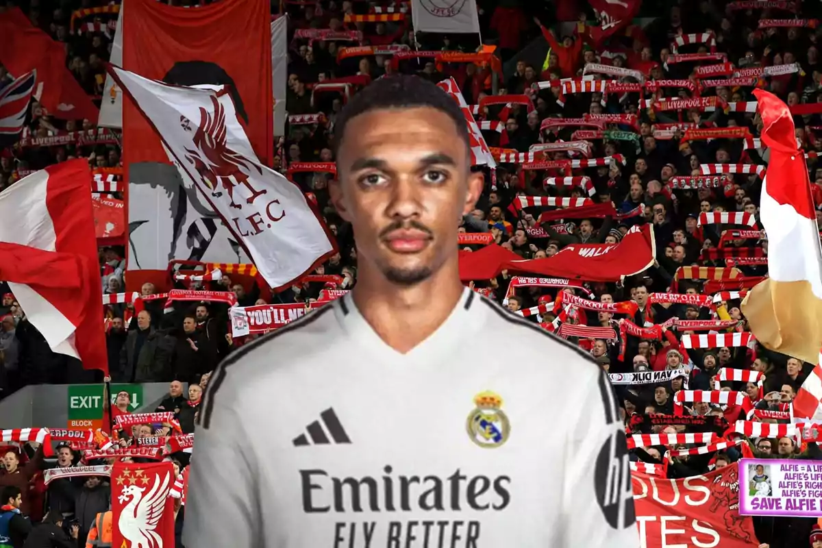Un jugador de fútbol con una camiseta blanca está frente a una multitud de aficionados que sostienen banderas y bufandas rojas del Liverpool.