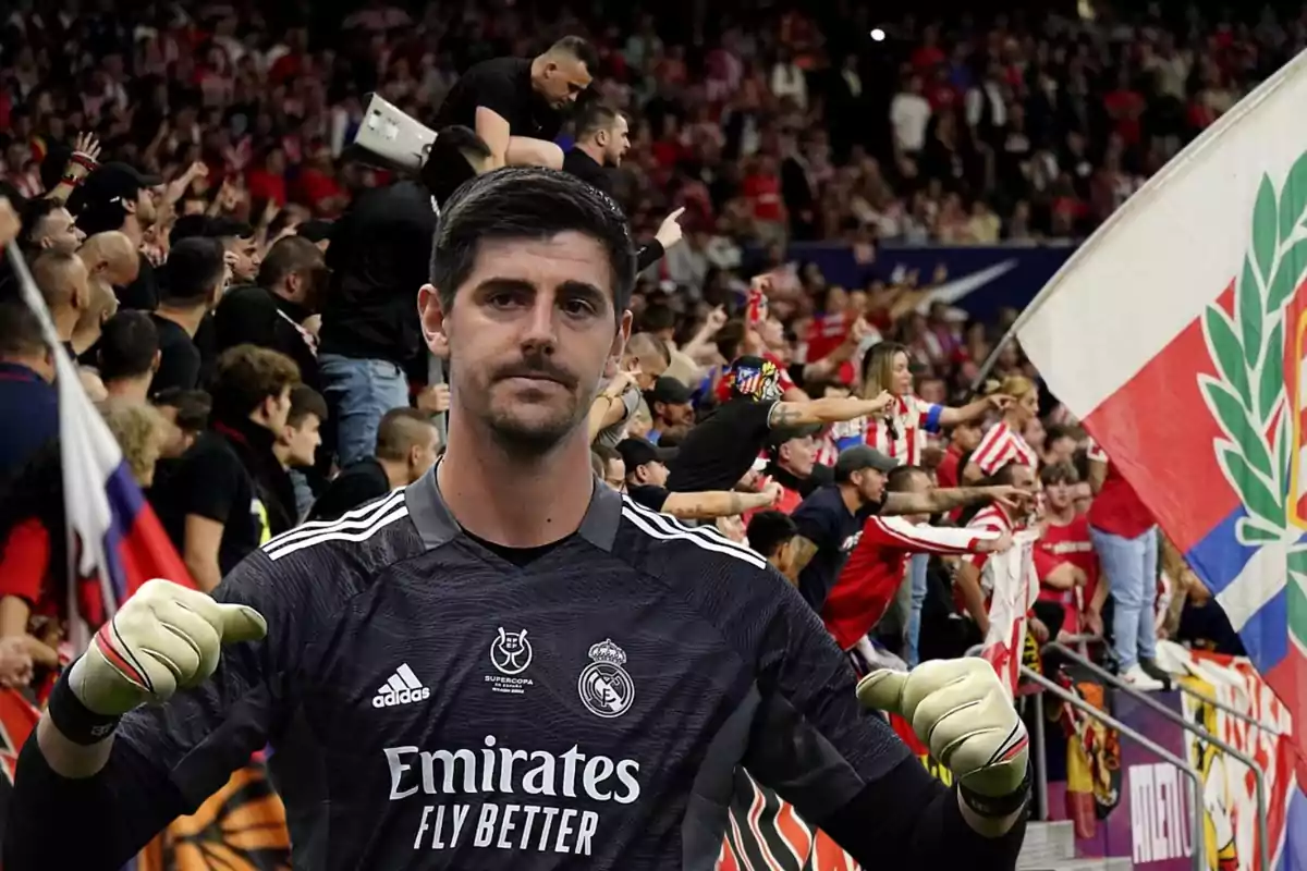 Un jugador de fútbol con uniforme oscuro está frente a una multitud de aficionados que agitan banderas y visten camisetas a rayas rojas y blancas.