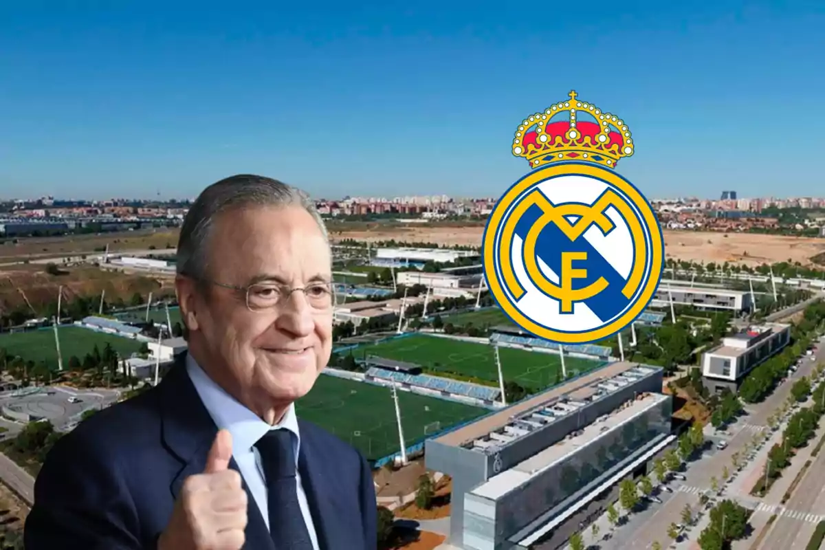 Un hombre con gafas y traje sonríe y levanta el pulgar frente a un complejo deportivo con el escudo del Real Madrid.