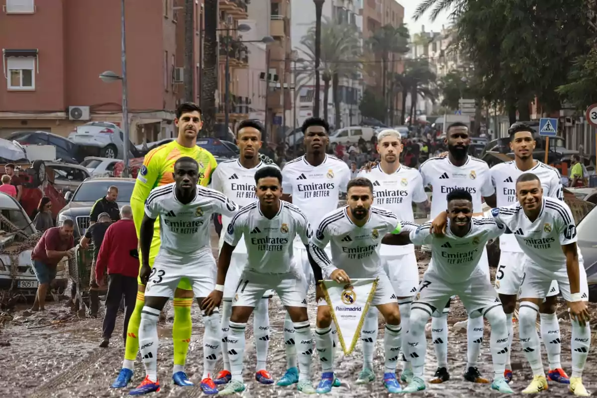 Un equipo de fútbol posando en una calle con coches dañados y personas caminando entre el barro.