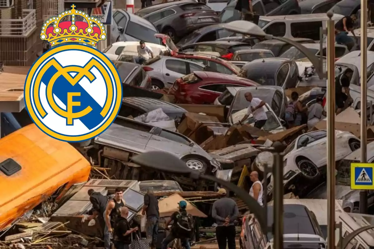 Un grupo de personas observa una gran cantidad de autos apilados y dañados en una calle, con el logo del Real Madrid superpuesto en la esquina superior izquierda.