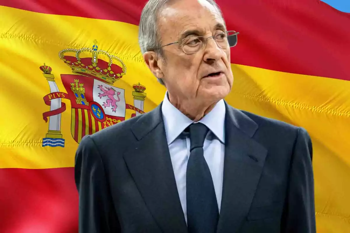 Un hombre mayor con gafas y traje oscuro frente a una bandera de España.