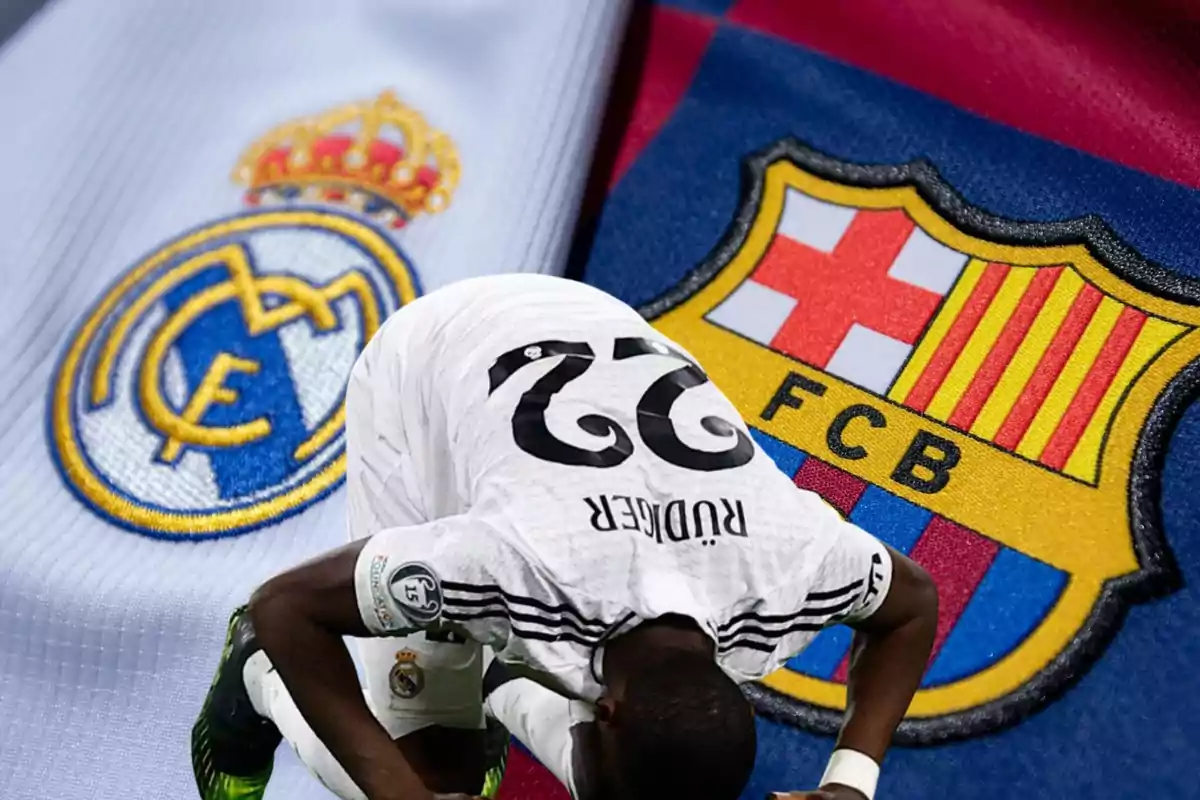 Un jugador de fútbol con la camiseta blanca se inclina frente a los escudos de los equipos Real Madrid y Barcelona.