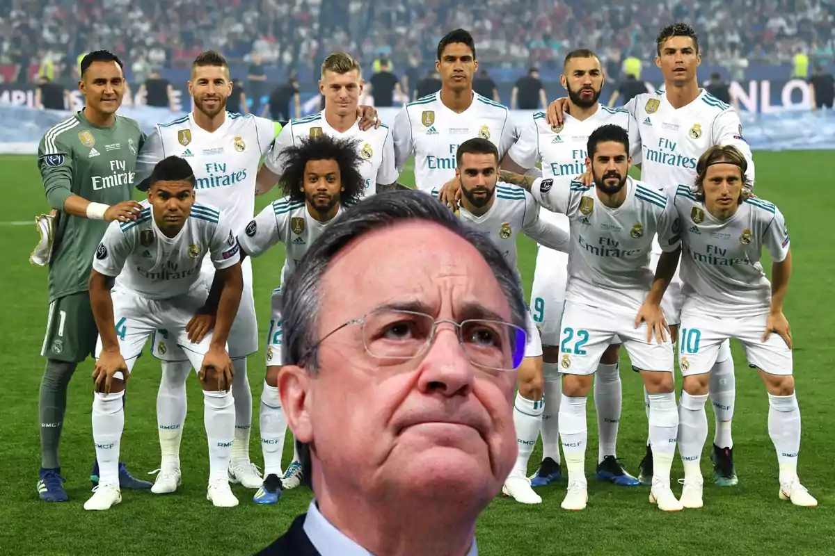 Un grupo de jugadores de fútbol con uniforme blanco posando en el campo mientras un hombre con gafas aparece en primer plano.