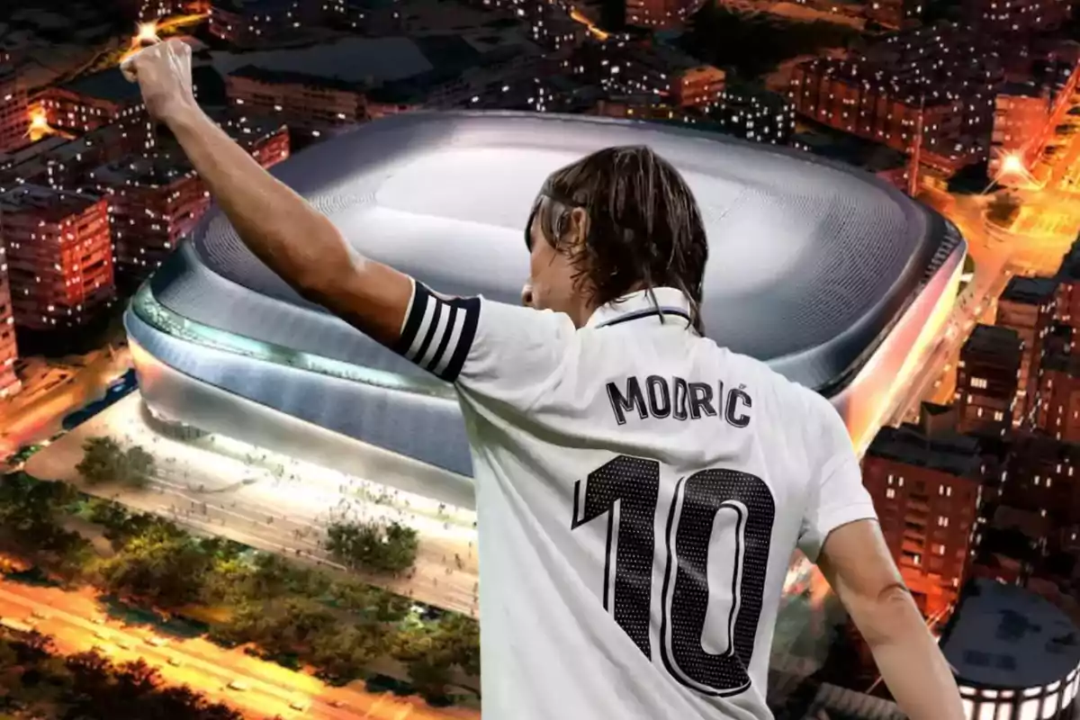 Un jugador de fútbol con el número 10 en su camiseta levanta el brazo frente a un estadio moderno iluminado por la noche.