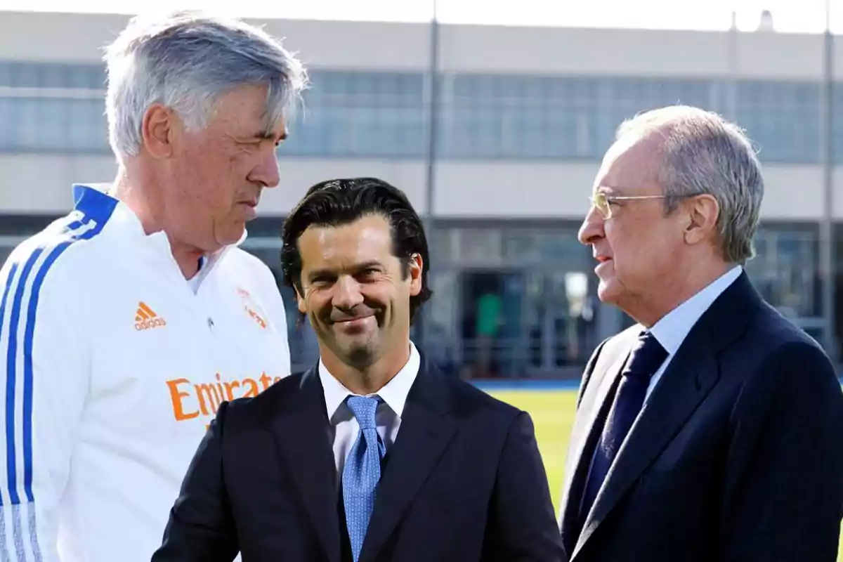 Tres hombres conversando en un campo de entrenamiento de fútbol.