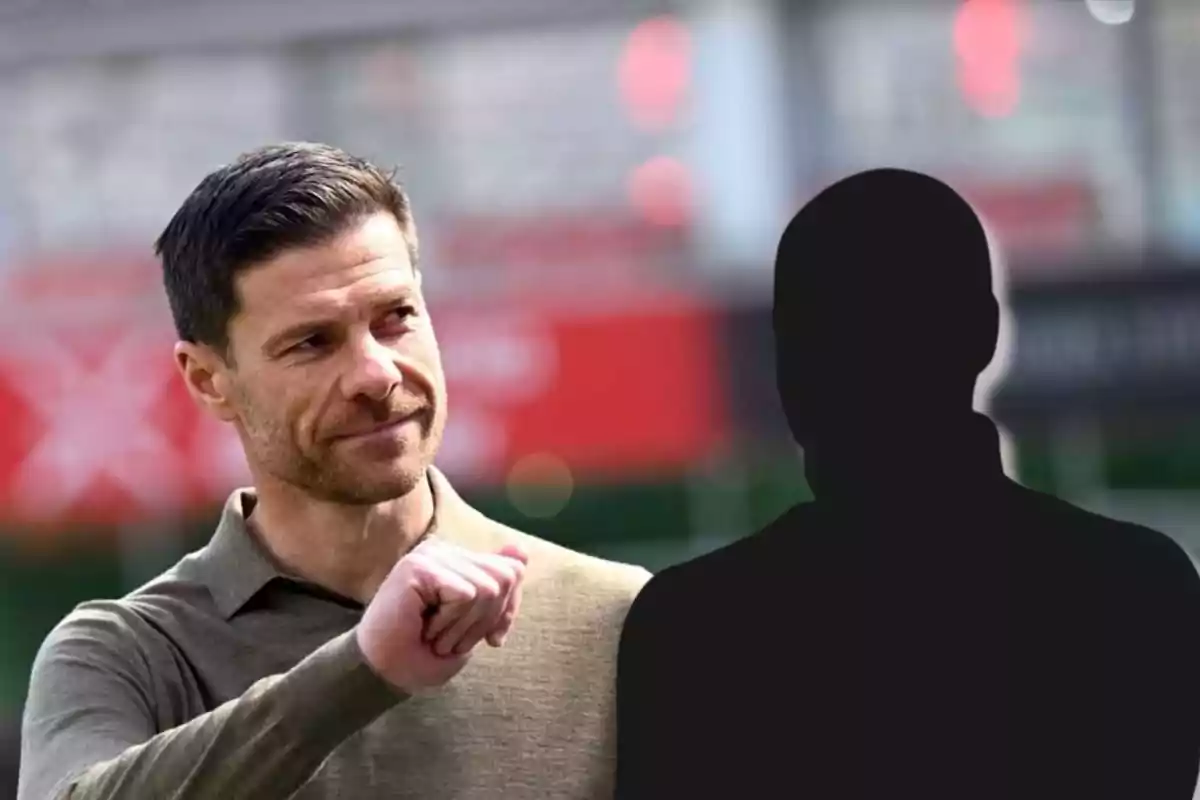 Un hombre sonriente con barba y cabello corto mira hacia un lado mientras hace un gesto con la mano, junto a una silueta negra de una persona sobre un fondo desenfocado.