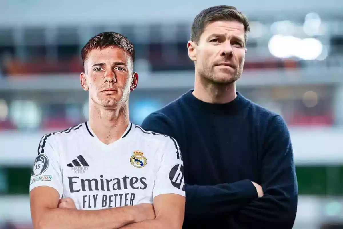 Dos hombres posan juntos, uno lleva el uniforme blanco del Real Madrid y el otro viste un suéter oscuro, ambos con expresión seria y fondo desenfocado de estadio.