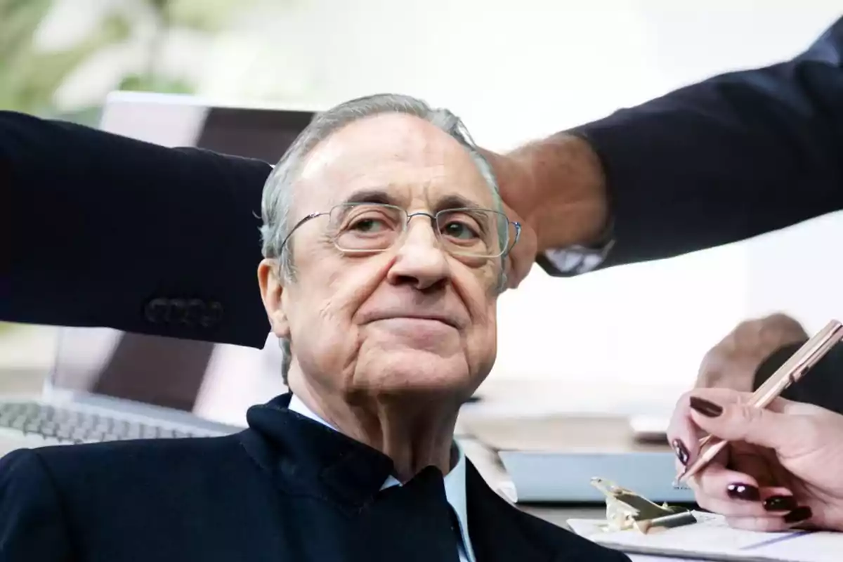 Hombre mayor con gafas y expresión seria al frente de una mesa de trabajo donde varias personas escriben y usan una computadora portátil