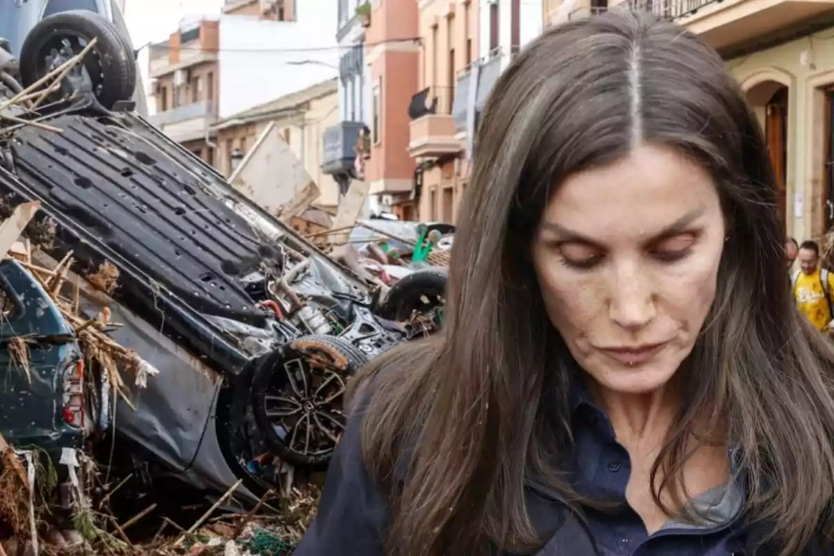 Una mujer con expresión seria está en una calle donde se observa un coche volcado y escombros alrededor.