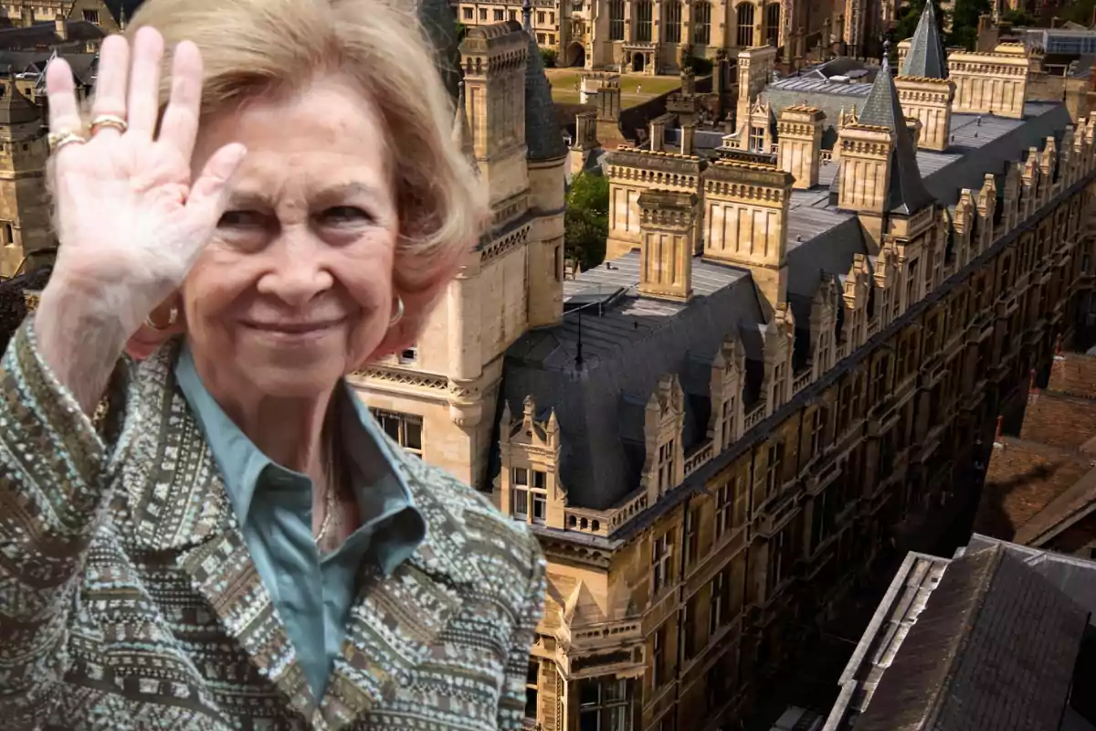 Una mujer mayor sonriente saluda frente a un edificio histórico con arquitectura gótica.