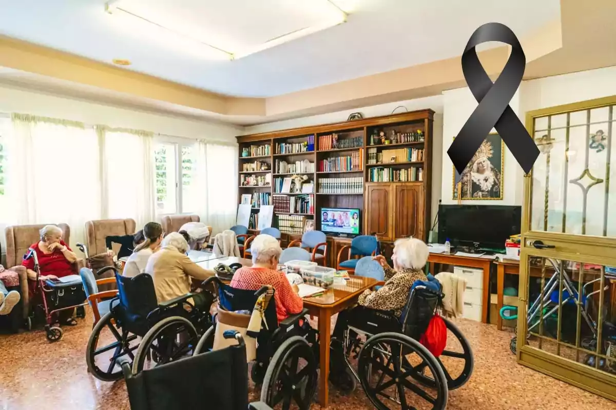 Personas mayores en sillas de ruedas en una sala común de una residencia con un lazo negro en la pared.