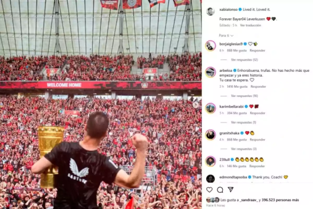 Un hombre de espaldas sostiene un trofeo dorado frente a una multitud de aficionados en un estadio, con un cartel que dice Un hombre de espaldas sostiene un trofeo dorado frente a una multitud de aficionados en un estadio, con un cartel que dice