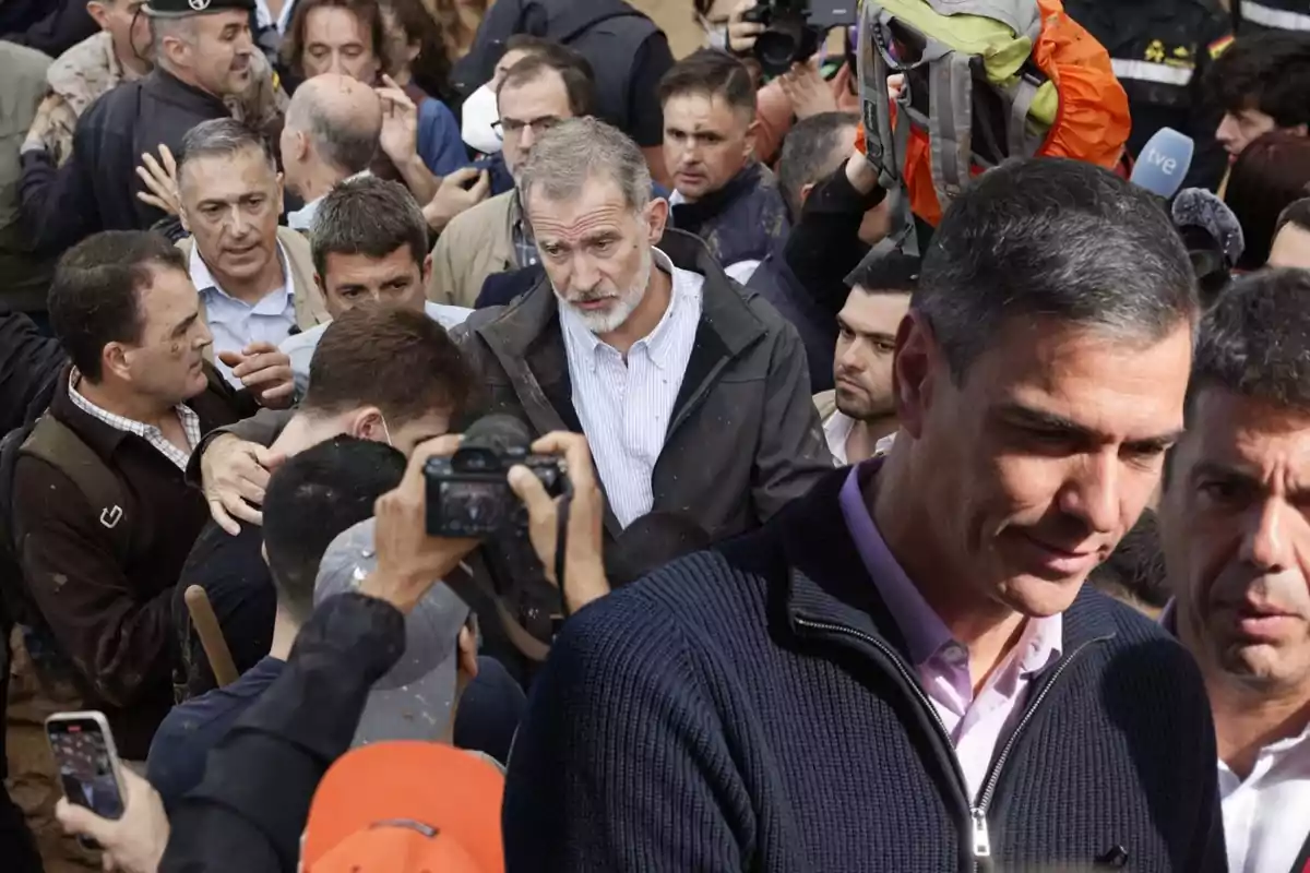 Un grupo de personas se encuentra reunido en un evento al aire libre, rodeados de cámaras y periodistas.