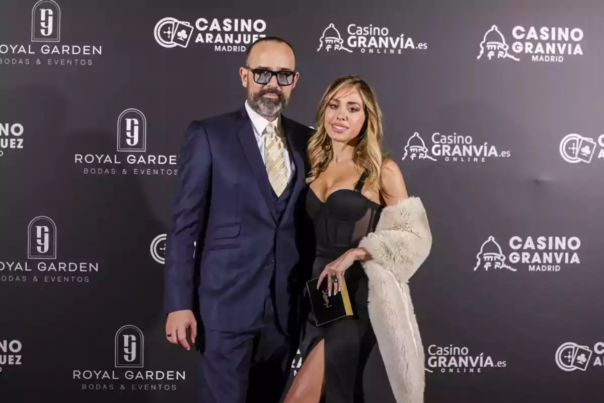 Una pareja posando en un evento elegante con un fondo que muestra logotipos de Casino Gran Vía y Royal Garden.