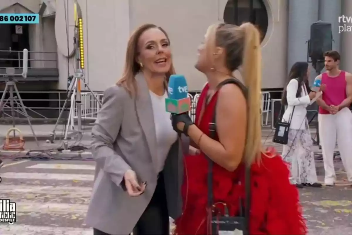 Dos mujeres están en una entrevista en la calle, una de ellas sostiene un micrófono de TVE mientras que al fondo se observa a otra reportera entrevistando a un hombre con camiseta sin mangas. Dos mujeres están en una entrevista en la calle, una de ellas sostiene un micrófono de TVE mientras que al fondo se observa a otra reportera entrevistando a un hombre con camiseta sin mangas.