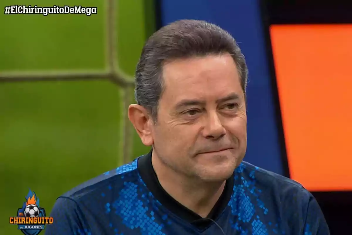 Un hombre con cabello corto y canoso, vestido con una camiseta azul con patrones geométricos, aparece en un programa de televisión llamado "El Chiringuito de Jugones".