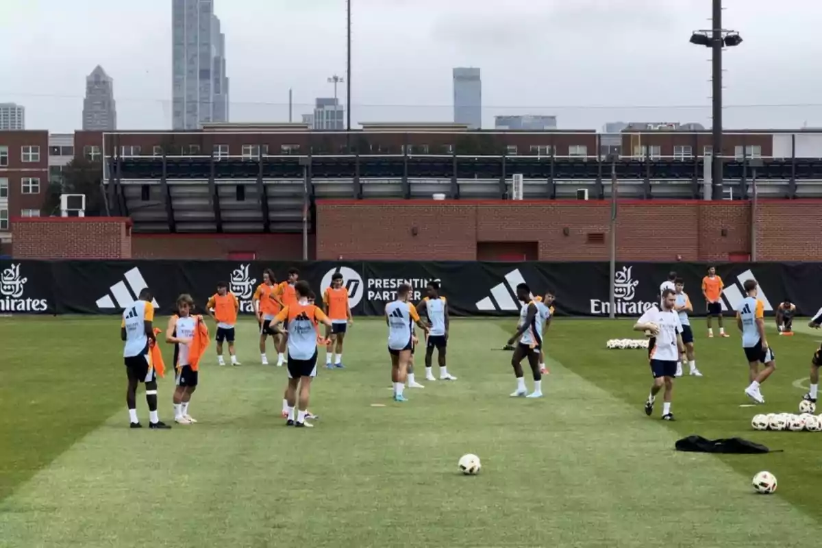 Jugadores de fútbol entrenando en un campo con edificios de fondo.