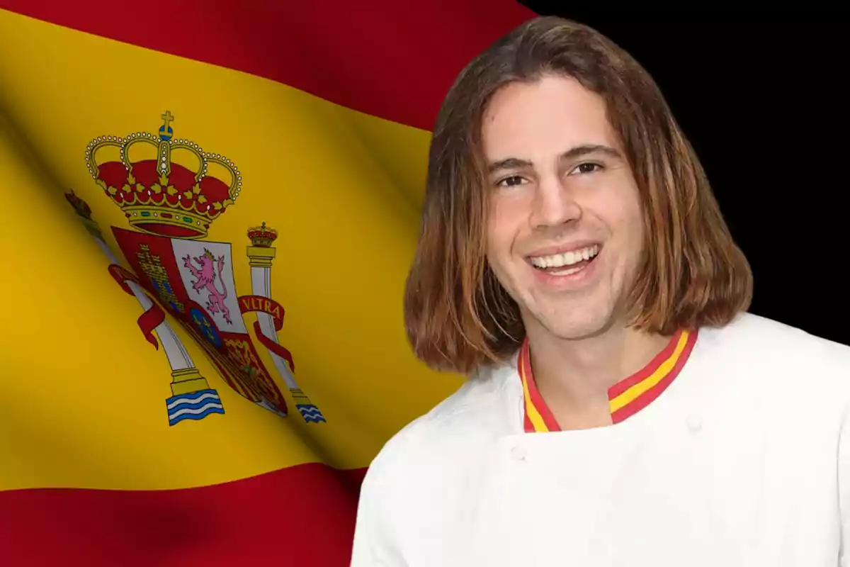 Persona sonriendo con una chaqueta blanca de chef frente a una bandera de España ondeando.