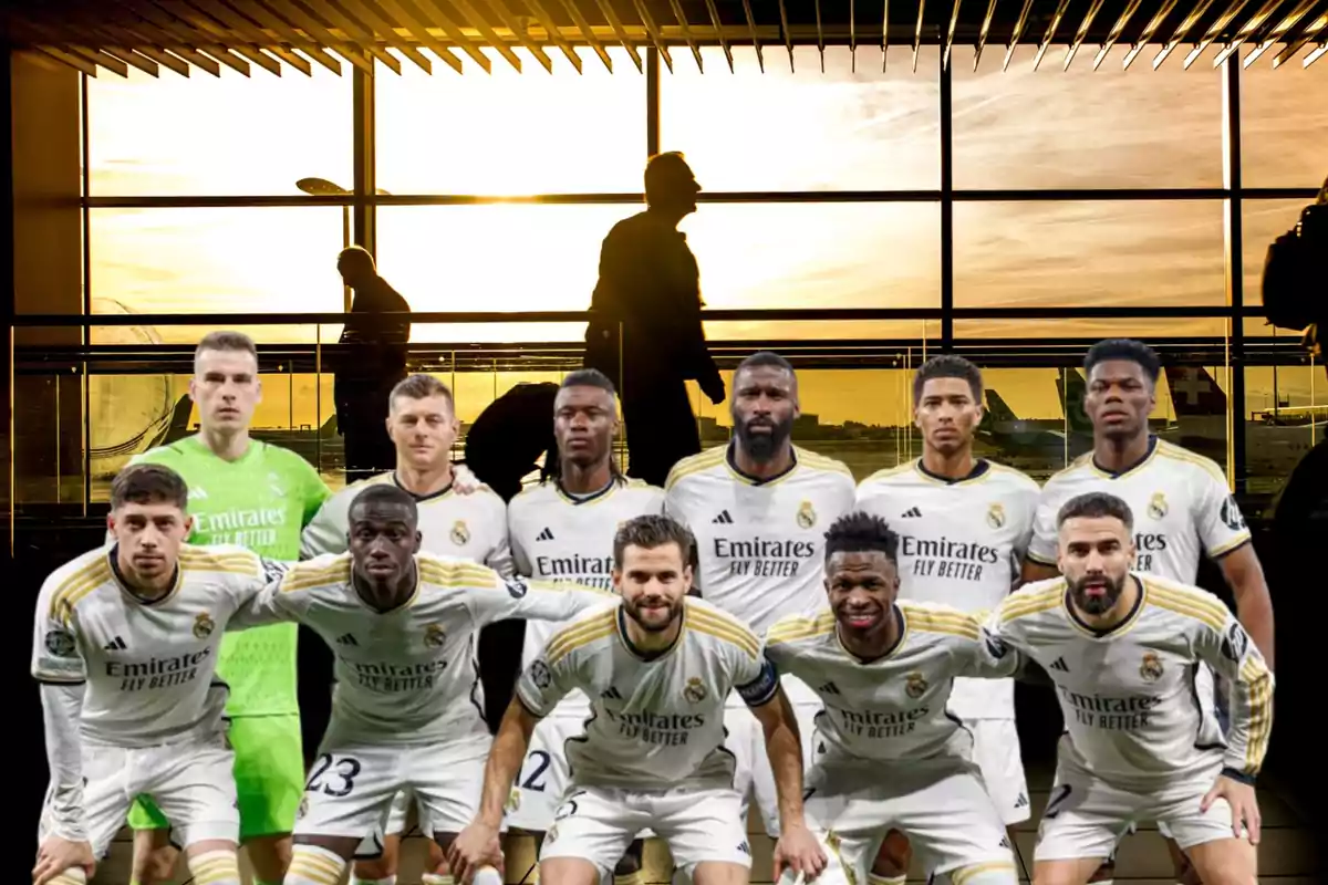 Jugadores de fútbol del Real Madrid posando para una foto grupal en un aeropuerto con un atardecer de fondo.