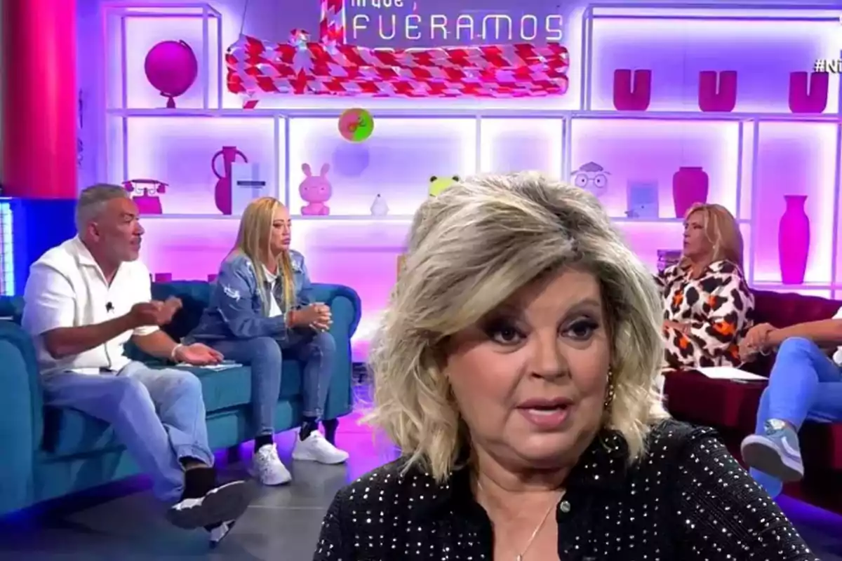 Un grupo de personas está participando en un programa de televisión con un set colorido y moderno, donde una mujer rubia en primer plano parece estar hablando mientras los demás la escuchan atentamente.