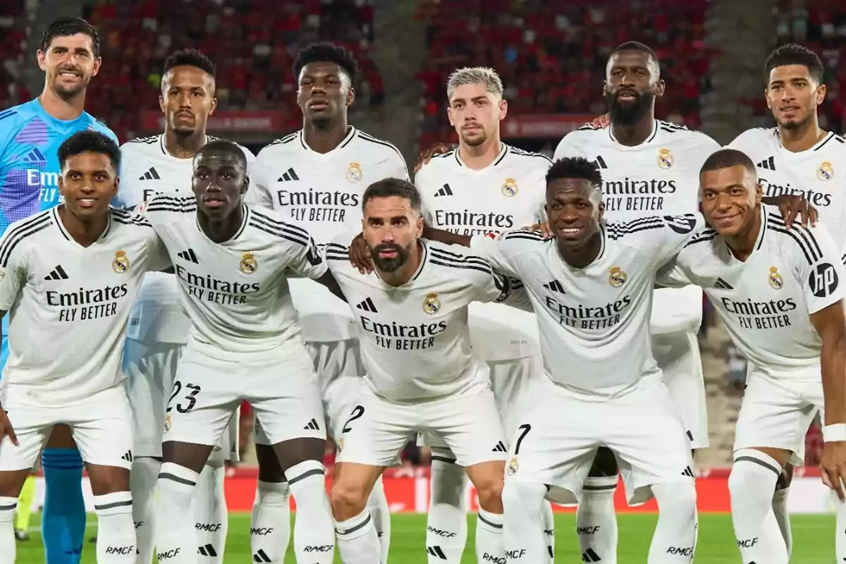 Un equipo de fútbol posando para una foto antes de un partido, todos los jugadores llevan uniformes blancos con el logo de "Emirates Fly Better".