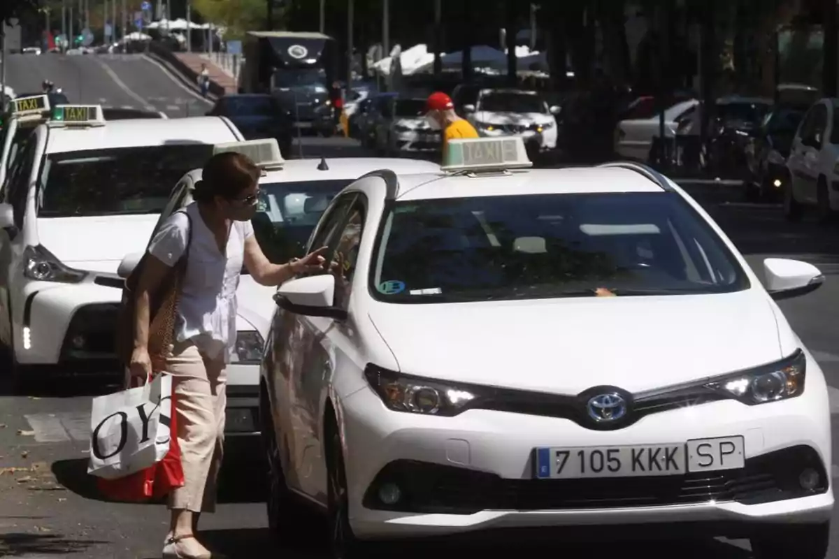 Una mujer se acerca a un taxi blanco en una calle concurrida.