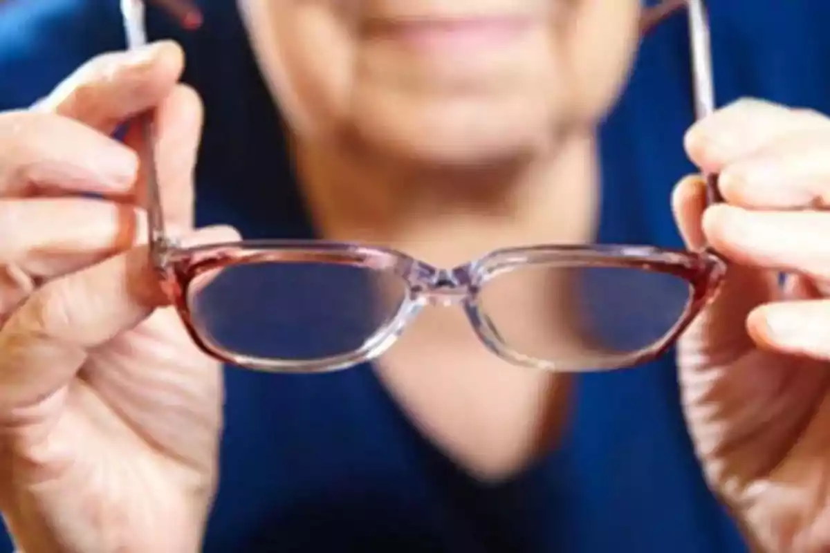 Una persona sosteniendo un par de gafas frente a su rostro.