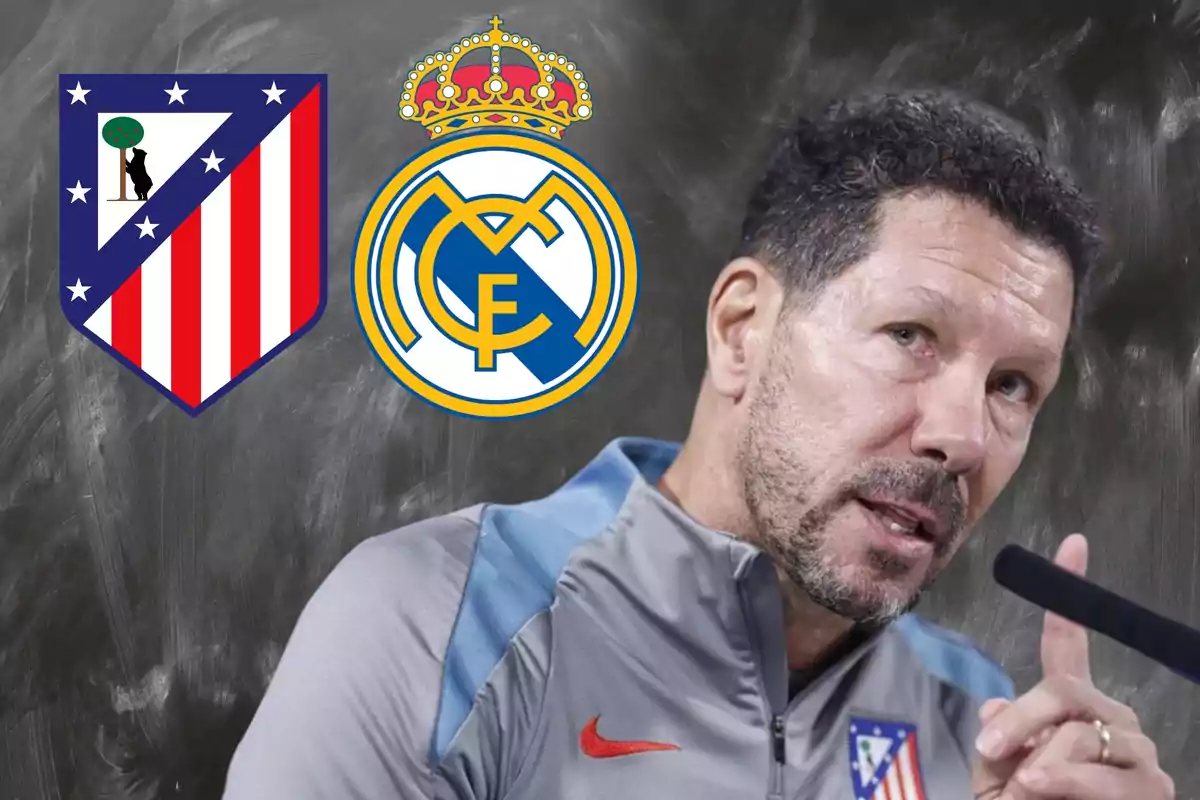 Un entrenador de fútbol hablando en una conferencia de prensa con los escudos del Atlético de Madrid y el Real Madrid en el fondo.