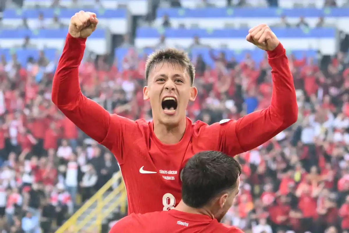 Arda Güler celebra con los brazos en alto mientras grita, con una multitud de aficionados en el fondo.