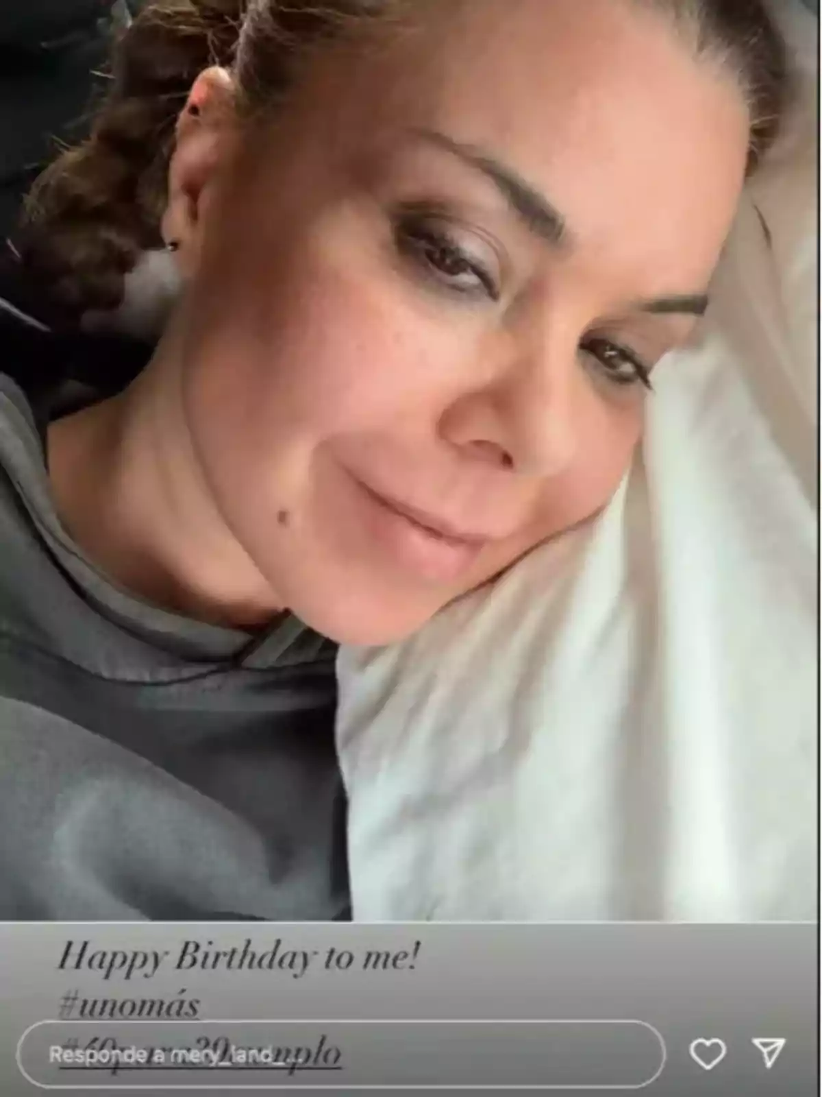 Mujer recostada sobre una almohada blanca con expresión relajada y maquillaje suave, usando una sudadera gris y con el cabello recogido. Mujer recostada sobre una almohada blanca con expresión relajada y maquillaje suave, usando una sudadera gris y con el cabello recogido.
