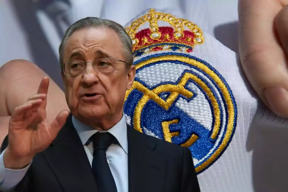 Un hombre con gafas y traje oscuro gesticulando con la mano frente a un escudo del Real Madrid.