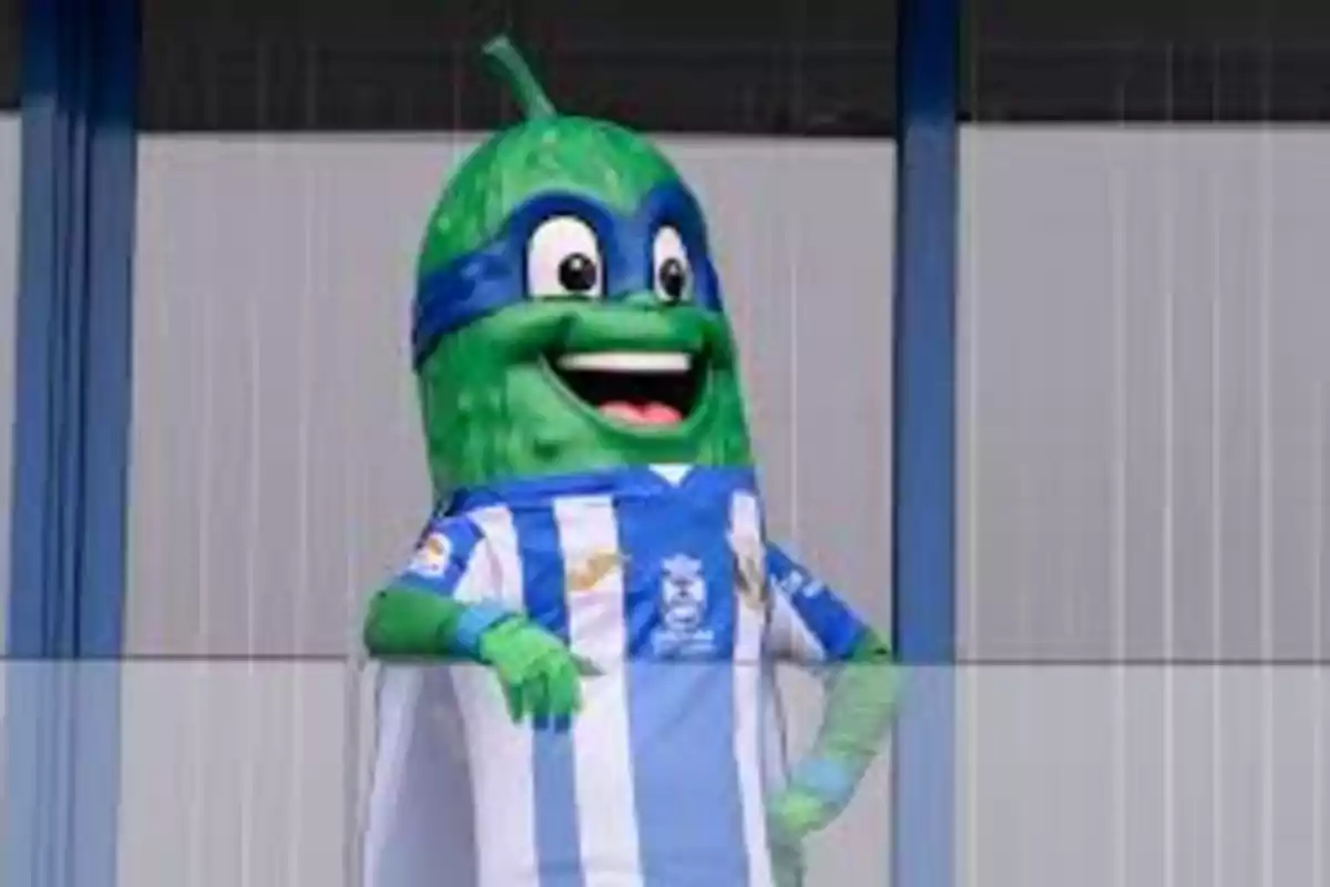 Mascota disfrazada de pepino con camiseta de rayas azules y blancas sonriendo alegremente.