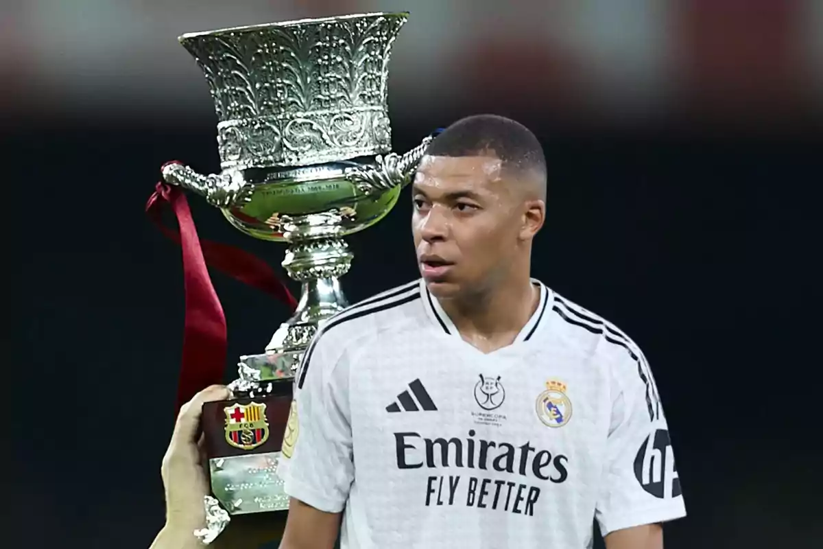 Un jugador de fútbol con la camiseta del Real Madrid aparece frente a un trofeo grande y decorado.