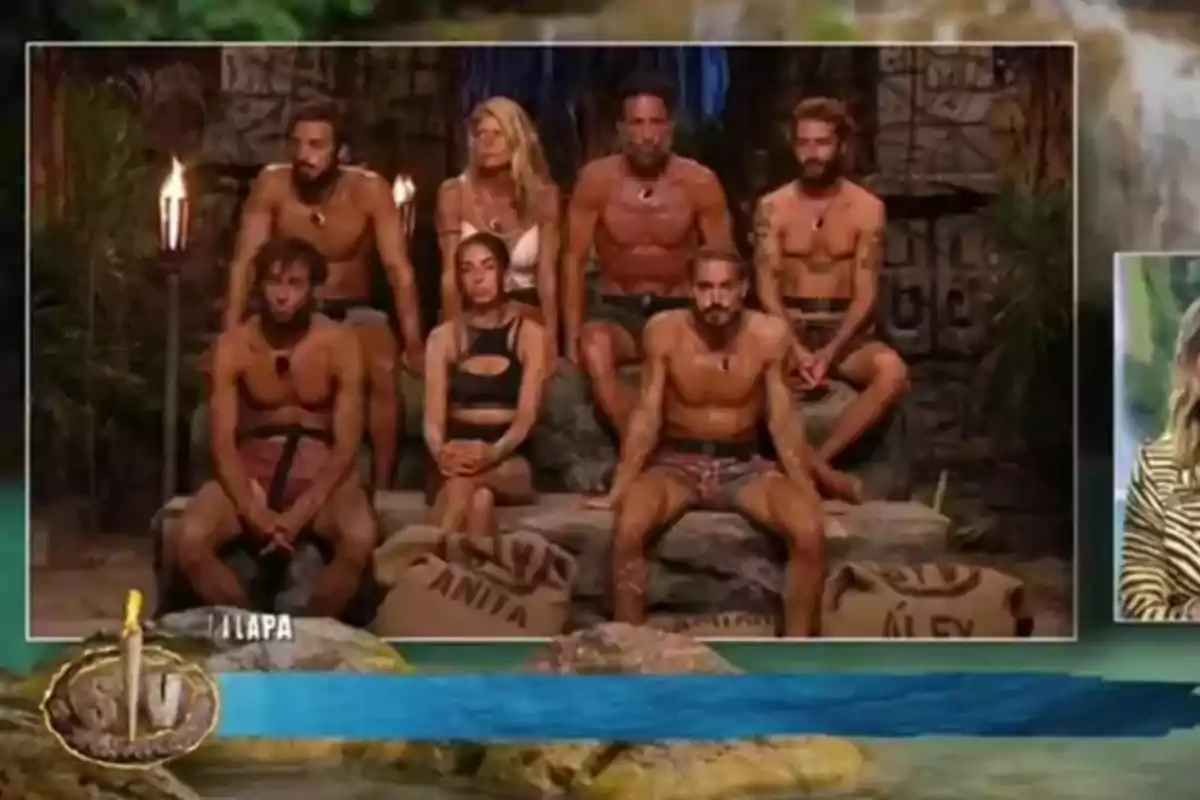 Siete personas con ropa de playa están sentadas en una especie de cueva decorada con antorchas y sacos, en lo que parece ser un programa de telerrealidad de supervivencia. Siete personas con ropa de playa están sentadas en una especie de cueva decorada con antorchas y sacos, en lo que parece ser un programa de telerrealidad de supervivencia.