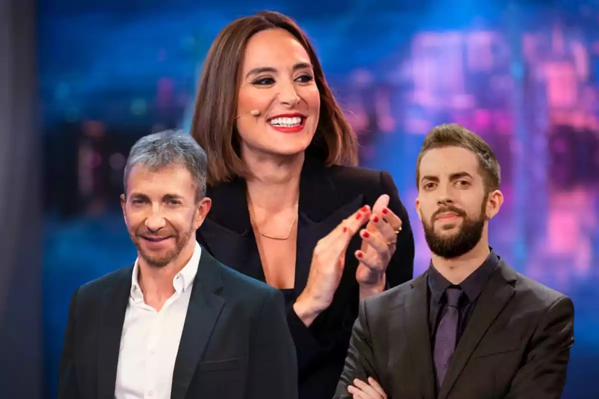 Tres personas posando y sonriendo en un set de televisión con fondo borroso.