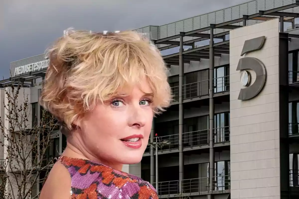 Una mujer rubia con cabello corto y rizado, vestida con un atuendo colorido, posa frente a un edificio con el logotipo de Mediaset España y el número 5.