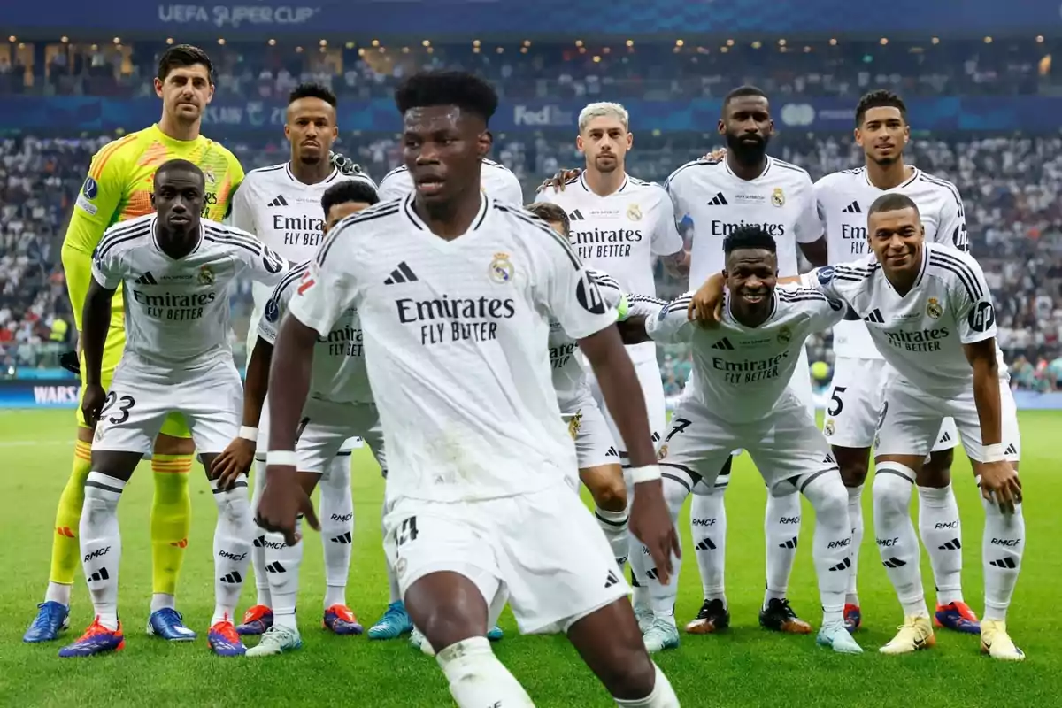 Jugadores de fútbol del Real Madrid posando en el campo antes de un partido con uniformes blancos y fondo de estadio lleno de espectadores.