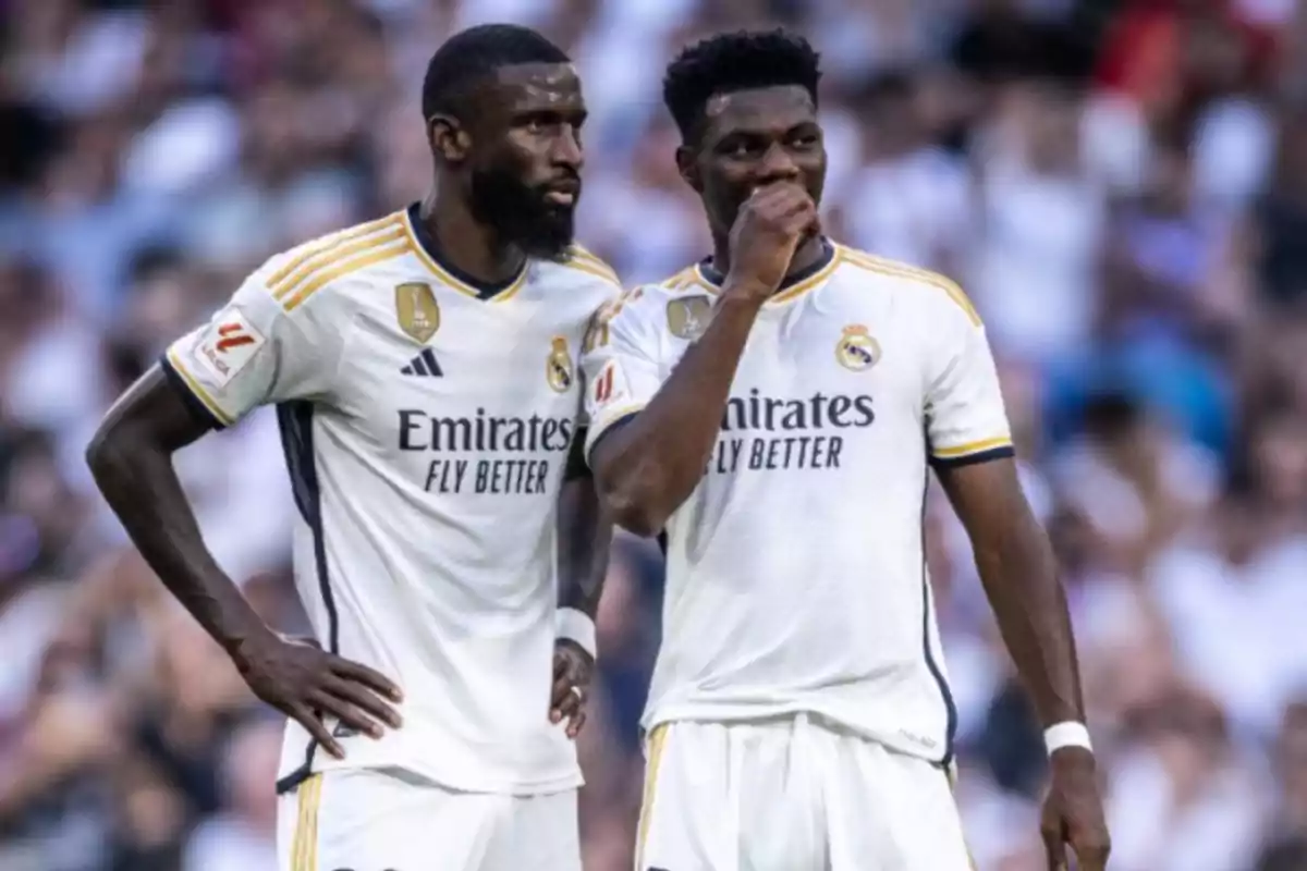 Dos jugadores del Real Madrid en el campo de fútbol con uniformes blancos.