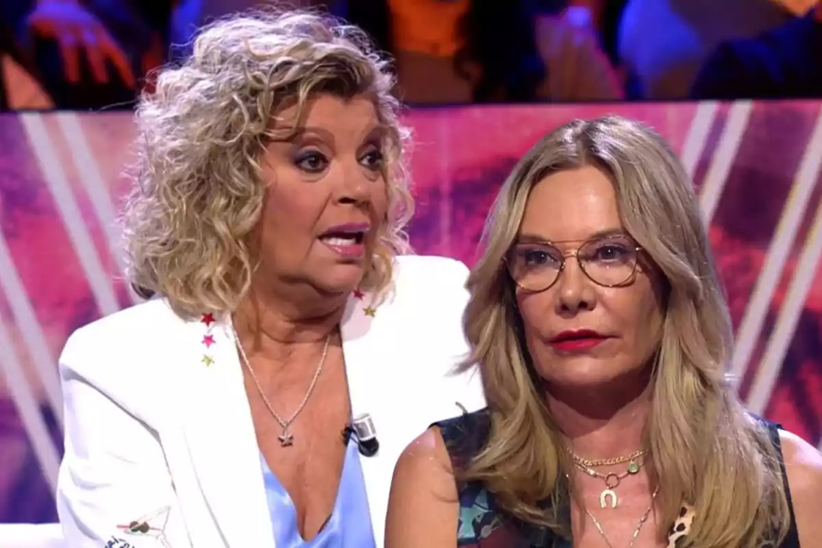 Dos mujeres sentadas en un plató de televisión con expresiones serias y fondo colorido