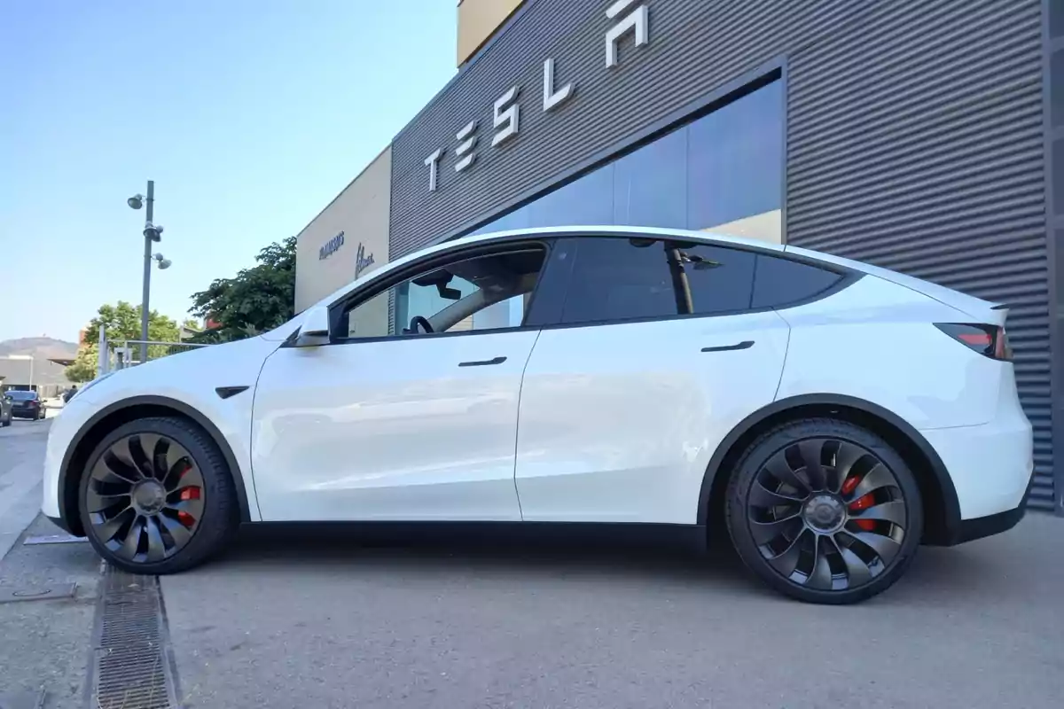 Coche eléctrico blanco estacionado frente a un edificio de Tesla Coche eléctrico blanco estacionado frente a un edificio de Tesla