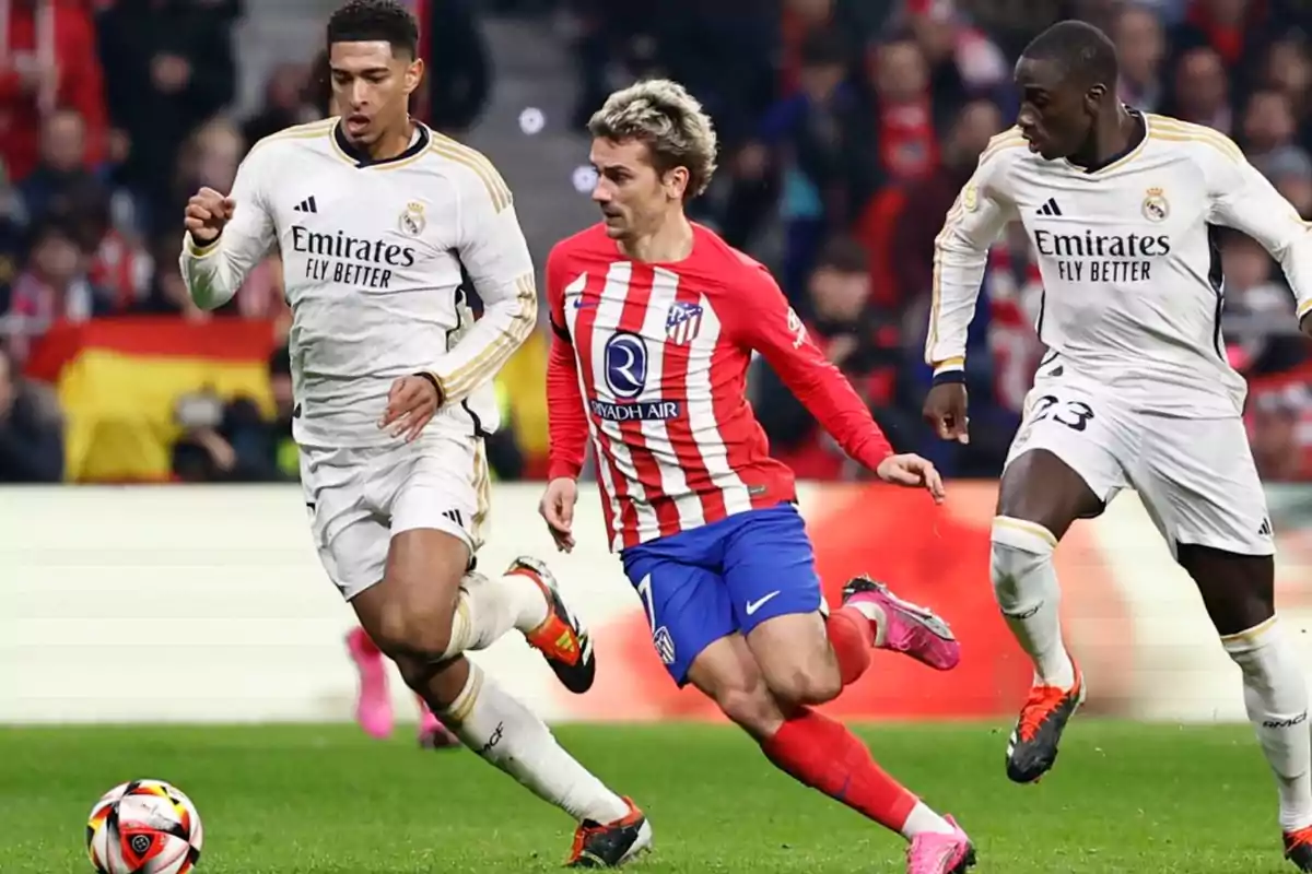 Jugadores de fútbol de los equipos Real Madrid y Atlético de Madrid compitiendo por el balón en un partido.