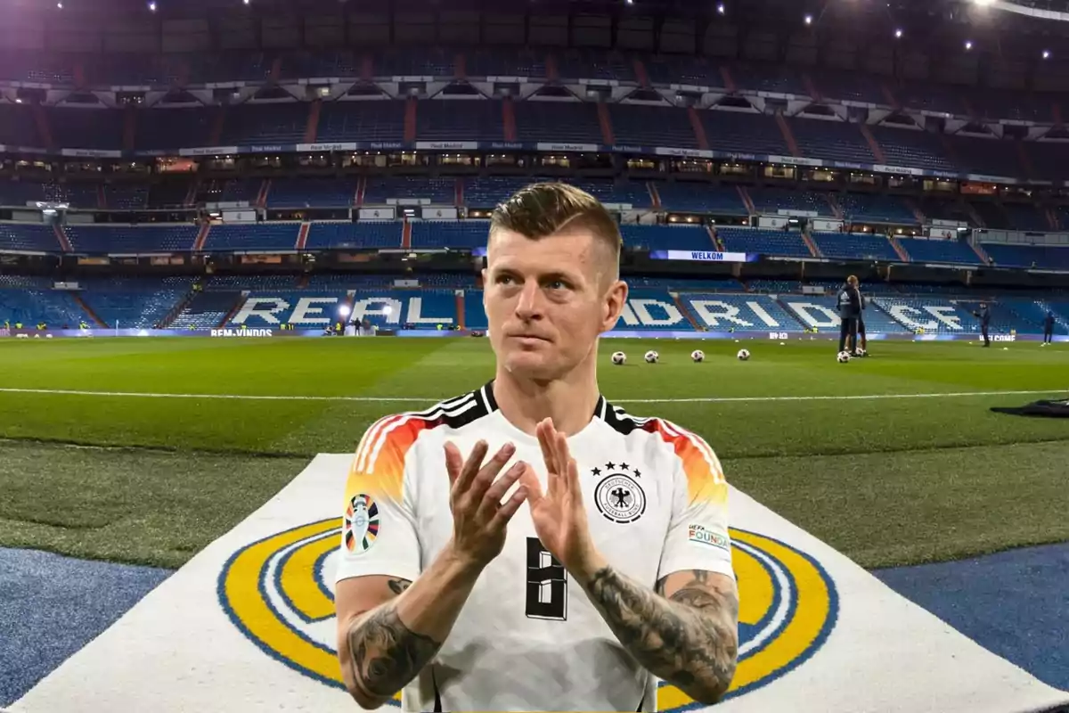 Un jugador de fútbol con la camiseta de la selección alemana aplaude en un estadio vacío con el logo del Real Madrid en el césped.