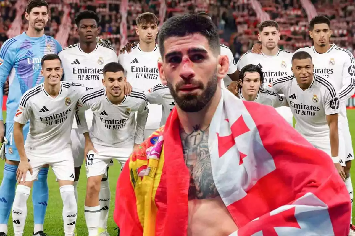 Un grupo de jugadores de fútbol con uniformes blancos posando en el campo, mientras un hombre con una bandera sobre los hombros está en primer plano.