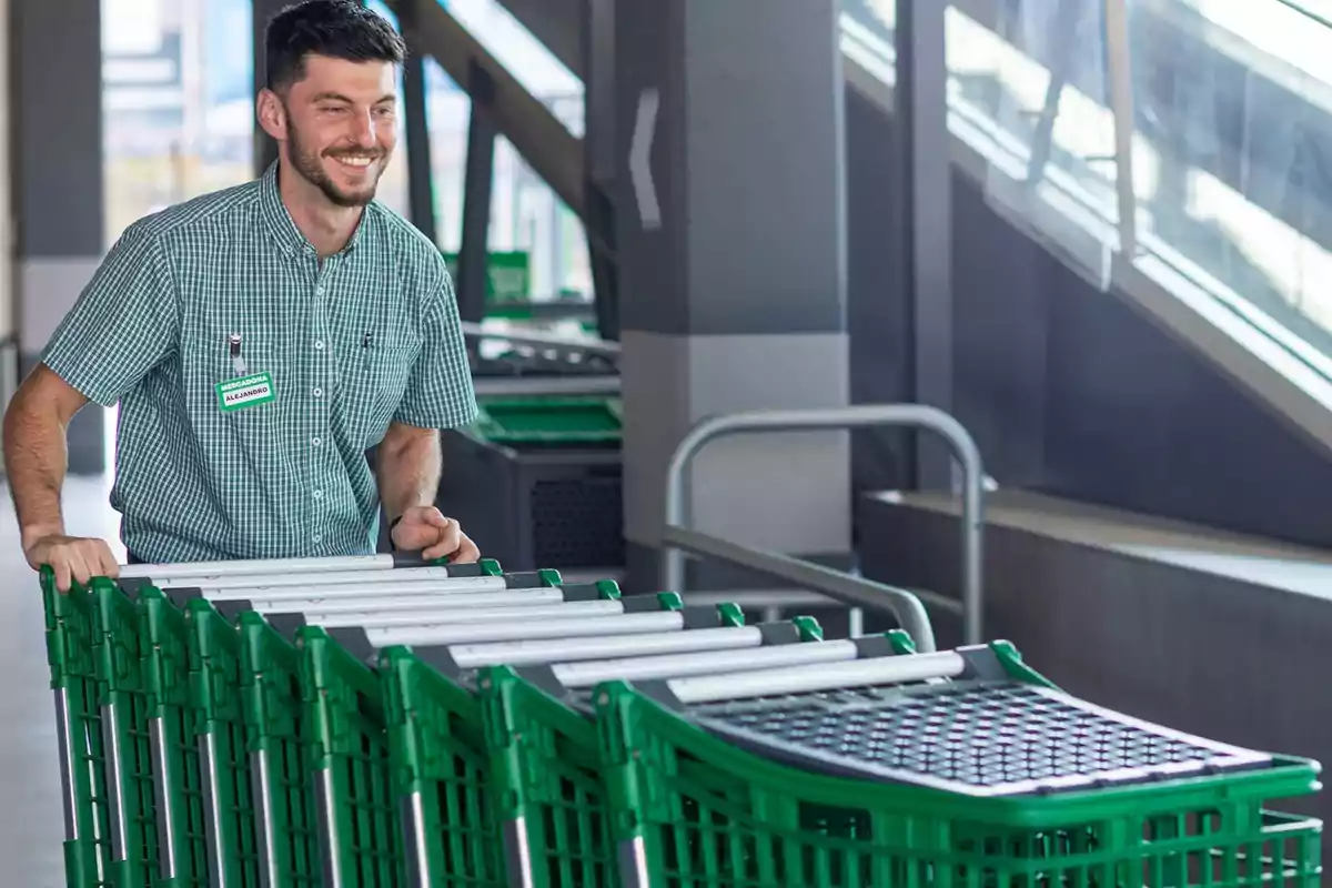 Un hombre sonriente empuja una fila de carritos de supermercado en un entorno interior.